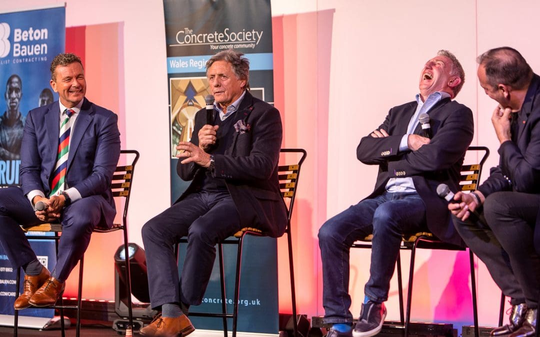 Four men sitting on stage at a business event, with one man laughing, creating a lively and engaging atmosphere.