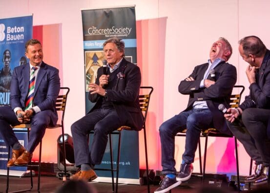 Four men sitting on stage at a business event, with one man laughing, creating a lively and engaging atmosphere.